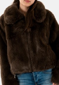 Giacca in finta pelliccia marrone con una texture morbida, design corto e colletto oversize, abbinata a jeans di denim blu.