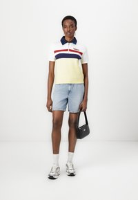 Polo skjorte i hvid og gul med marineblå og røde striber, parret med lyse denim shorts og en sort taske, iført sølv sneakers og hvide strømper.