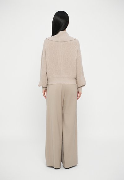 Beige strikket genser med bred krage, kombinert med løse taupe bukser. Stoffet ser strukturert ut med en avslappet passform og senkede skuldre.