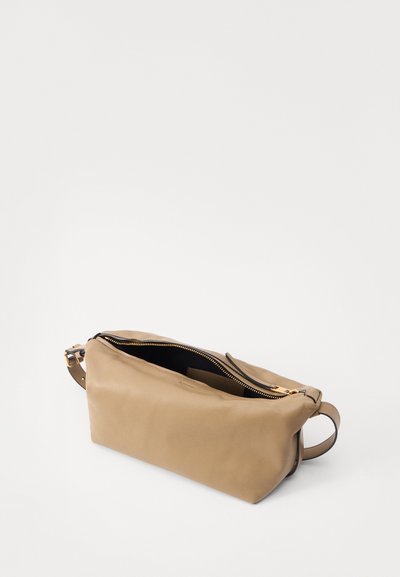 Sac en cuir tan avec une texture lisse, un dessus zippé et une poignée latérale, présentant des coutures minimales et un intérieur organisé.
