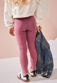 Roza leggingi iz mehkega materiala, v kombinaciji s kratkim krem puloverjem. Modra denim jakna prek roke. Bele superge z črnimi detajli.