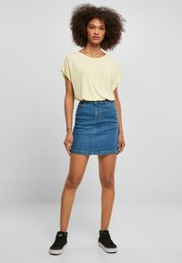 Gul kortærmet top parret med en blå denim miniskirt. Sorte high-top sneakers akkompagnerer outfittet. Enkel design med en afslappet pasform.