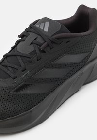Scarpe sportive nere con tomaia in rete, dettagli testurizzati e suola imbottita. Presentano tre strisce seghettate e lacci tondi.