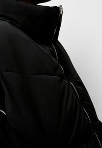 Black puffer jacket with a high collar, featuring a diagonal zipper. Material appears shiny with a smooth texture and stitched panel design.