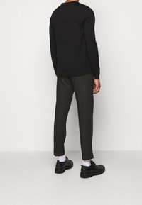 Pull noir à manches longues, associé à un pantalon gris fuselé et des chaussures noires, vu de dos sur fond blanc.