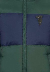 Giubbotto puffer verde e blu navy con una cerniera centrale e un accento del logo texturizzato. Presenta sezioni trapuntate e una finitura liscia.