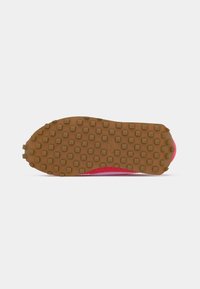 Sola de borracha castanha com padrão de piso quadrado numa sapatilha Nike rosa vista de baixo, contra um fundo branco.