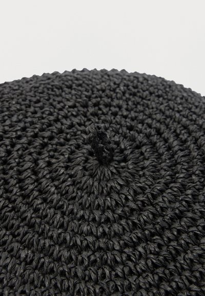 Κοντινό πλάνο μαύρου πλεκτού μπερέ, που δείχνει το υφασμένο κυκλικό σχέδιο πλέξης και τον κεντρικό βρόχο στην κορυφή.