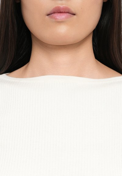 Top bianco a coste con scollatura ampia, texture liscia e delicata lucentezza, indossato da una persona con lunghi capelli scuri, che mostra un design pulito e minimalista.