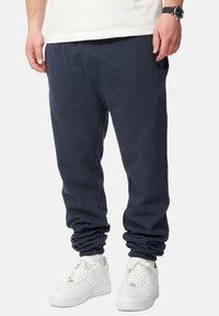 Navyblaue Sweatpants aus weichem Stoff mit einem lässigen Schnitt, ausgestattet mit elastischen Bündchen und Taschen, kombiniert mit weißen Sneakers.