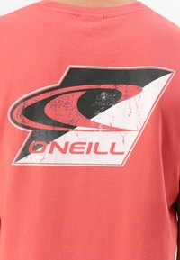 Back of a red t-shirt with a large black and white O'Neill logo featuring a stylized wave and text, slightly worn and faded.