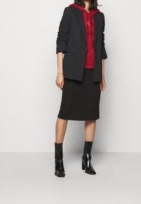 Black tailored blazer over a red hoodie, paired with a black midi skirt and shiny black ankle boots. Minimalist design with a relaxed fit.