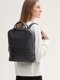 Czarny skórzany plecak z gładką górną częścią i teksturowanym dolnym fragmentem. Posiada podwójne uchwyty, regulowane szelki oraz przednią kieszeń na zamek.