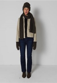 Beige jakke, sort top, mørkeblå jeans, brune handsker, tørklæde og hat. Materialerne er bløde, og hatten har et tekstureret strikkemønster.