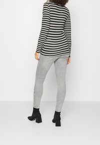 Top de manga larga a rayas negras y grises con dobladillo redondeado, combinado con jeans ajustados gris claro y botines con tacón bloque negro.