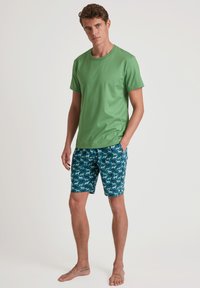 Groene katoenen t-shirt gecombineerd met blauwe shorts met een patroon van witte honden. Het t-shirt heeft een ronde halslijn en korte mouwen.