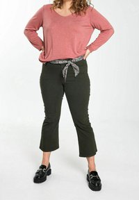 Top rosa a maniche lunghe con scollo a V profondo, abbinato a pantaloni cropped verde scuro con cintura a fiocco a stampa floreale. Mocassini neri con plateau.