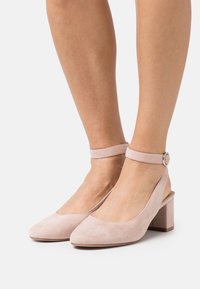 Pink suede slingback heels with a pointed toe, ankle strap, and 5 cm block heel; smooth texture with minimal design details.