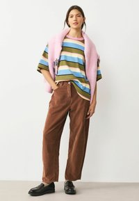 Proužkované bavlněné tričko v modré, zelené a růžové barvě, kombinované s hnědými manšestrovými kalhotami s širokými nohavicemi a černými mokasínami, doplněné růžovým svetrem.