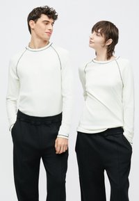 Valged pikad varrukad hallide õmblusdetailidega, kombineeritud mustade lahtiste pükstega, millel on elastne vöökoht. Sile kangapind.