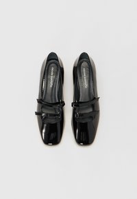 Black patent leather Mary Jane shoes with a square toe, featuring two narrow straps with buckles, smooth texture, and contrasting interior.