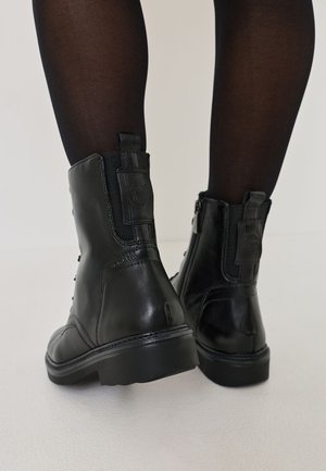 Black leather ankle boots with a textured upper, zipper closure, round toe, and a sturdy rubber outsole. Features a logo detail on the back.