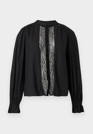 Blouse noire à manches longues avec poignets froncés, col montant, et panneau vertical en dentelle florale avec ruban en velours noué au centre devant.