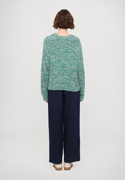 Green textured knitted sweater with long sleeves, relaxed fit, and wide neckline, paired with navy wide-leg trousers and light-colored shoes.