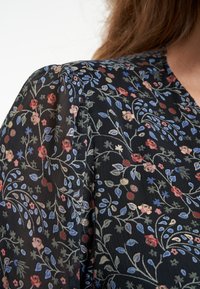 Tissu noir avec un motif floral comprenant des fleurs rouges, bleues et vertes. Surface texturée avec des rayures verticales subtiles.