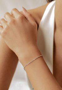 Pulsera de plata en una muñeca, con un diseño retorcido y pequeños detalles de acento, sobre un fondo neutro. Textura suave y brillo.