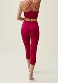 Sportowy stanik typu racerback oraz legginsy 3/4 w jaskrawym czerwonym kolorze. Gładka tekstura, dopasowany krój z widocznymi szwami i długość do kostek.