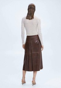 Bruine leren midi-rok met plooien, een gladde textuur, hoge taille en een achteropening. Gemaakt met een strak, lichtgekleurde lange mouw top.