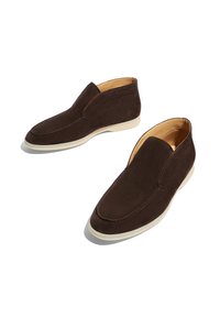 Un par de zapatos tipo slip-on de ante marrón oscuro con suelas de goma blanca, forro interior beige y detalles de costura en la parte superior.