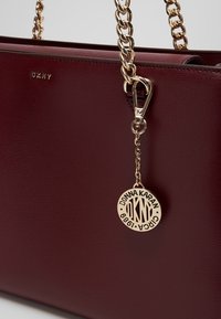 Sac à main en cuir bordeaux avec des anses en chaîne dorée et un pendentif circulaire avec le logo DKNY gravé "Donna Karan Circa 1989."