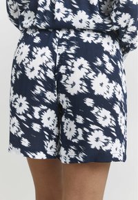 Shorts à motifs floraux bleu marine et blanc, fabriqués en tissu léger, offrant une coupe décontractée et une taille élastique pour le confort.