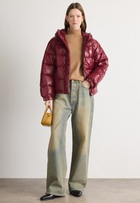 Burgunderfarget puffjakke med glanset finish, khaki genser med høy hals, vide lyseblå jeans og en liten gul håndveske. Svarte spisse sko.