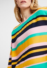Top a righe multicolori con linee orizzontali gialle, rosa, verdi e blu navy. Caratterizzato da un collo rotondo e una vestibilità ampia. Tessuto dalla texture liscia.
