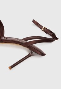 Brune sandaler med høye hæler og stropp, med et elegant design, spiss tå og en tynn ankelstropp med en gullspenne som detalj. Glatt tekstur.