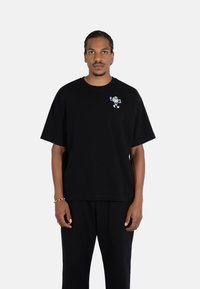 Black cotton t-shirt featuring a small, multicolored graphic on the chest. Loose fit with short sleeves and a crew neckline.