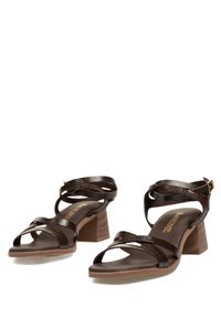 Las sandalias de tacón cuadrado de cuero marrón presentan tiras entrecruzadas, un acabado texturizado y una plantilla acolchada. Detalle de pequeña hebilla en tono dorado.