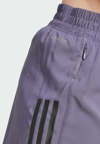 Lila Sportshorts aus leichtem Material, mit einem Reißverschlussfach, einem elastischen Bund und schwarzen Streifenakzenten.