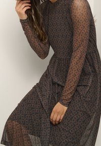 Durchsichtiges braunes Kleid mit einem gemusterten Design, langen Ärmeln, gerafftem Bund und fließendem Rock. Die Textur wirkt leicht und durchscheinend.