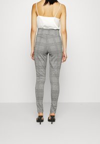 Grå rutiga högmidjade byxor med en åtsittande silhuett, slät textur och subtilt rutmönster, bärs med en vit satinlinne.