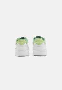 Fehér bőr sneaker zöld velúr díszítéssel a sarkon. Vastag fehér talppal és párnázott nyakkal rendelkezik a kényelem érdekében.
