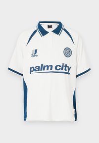 Άσπρο πόλο μπλουζάκι με μπλε λεπτομέρειες, με ριμπ κολάρο και κοντά μανίκια. Στο μπροστινό μέρος εμφανίζεται το κείμενο «palm city» με έντονα μπλε γράμματα.