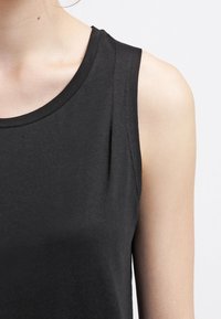 Top nero senza maniche con scollo tondo e una texture liscia e morbida. Presenta un leggero dettaglio plissettato sulla spalla.