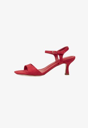 Sandalia de mujer de ante rojo con tacón bajo tipo 'kitten', puntera abierta y pulsera en el tobillo con hebilla sobre fondo blanco.