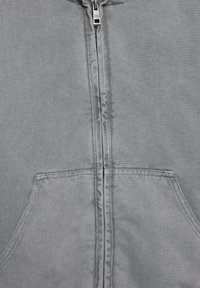 Graue Jacke zum Reißverschluss, hergestellt aus strukturiertem Stoff, mit einem mittigen Reißverschluss und einer Fronttasche, sichtbare Nähte entlang der Nähte.