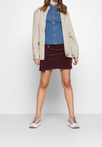 Beige kofta, denimskjorta, bourgognefärgad kordkjol med sidöppning och beige sneakers med vita och bruna detaljer.