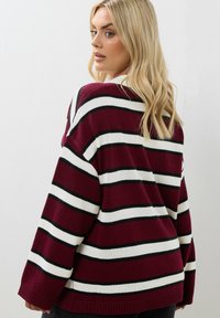 Vinröd- och vitrandig oversized tröja med svarta accenter, ribbat avslut och lös passform. Mjuk stickad material och design med sänkt axel.